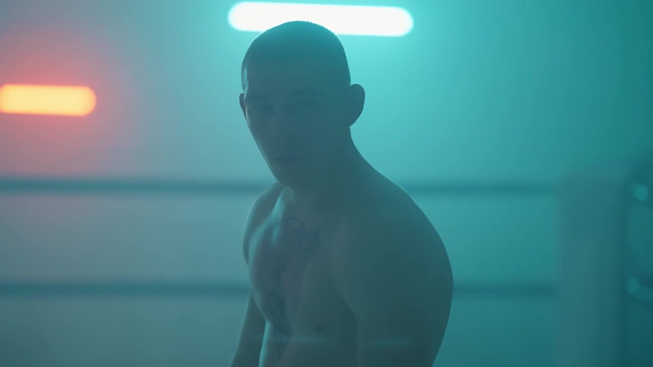 Serious Shirtless Man with Tattoo in Neon Lit Room