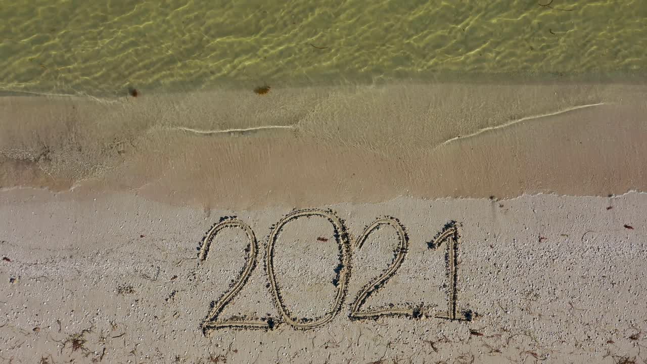 veinte veintiuno escrito en la arena en la parte inferior del marco mientras el agua cae a la playa