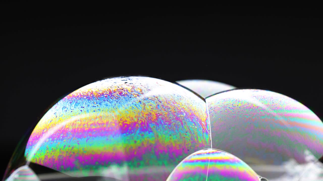 Vibrant soap bubbles display shifting colors against a dark background, highlighting iridescence and fluid dynamics in close-up view