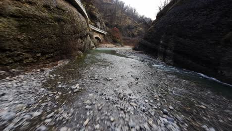 rushing river through a narrow rocky canyon with pebbled shore, captured in natural daylight, fpv shot