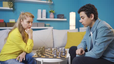 Concentrated-young-man-and-his-mother-playing-chess-at-home,-serious-and-focused.