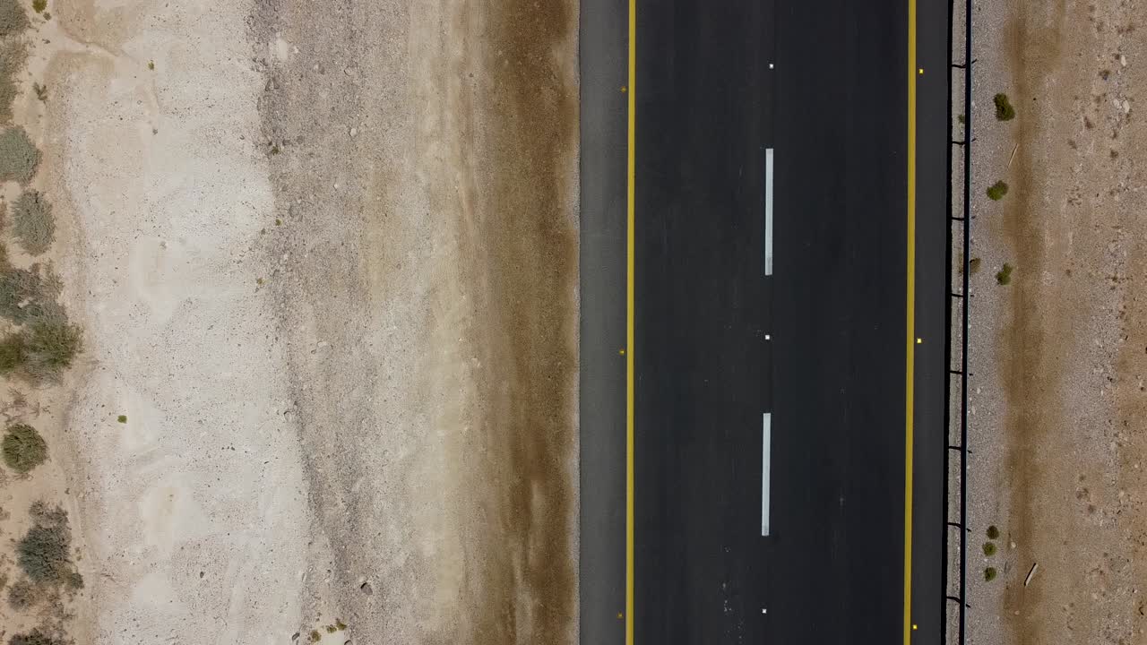 toma aérea estática de primer plano de un camión blanco que pasa rápido por una carretera en medio de un desierto israelí, rodeado de arena, suciedad y algunas plantas