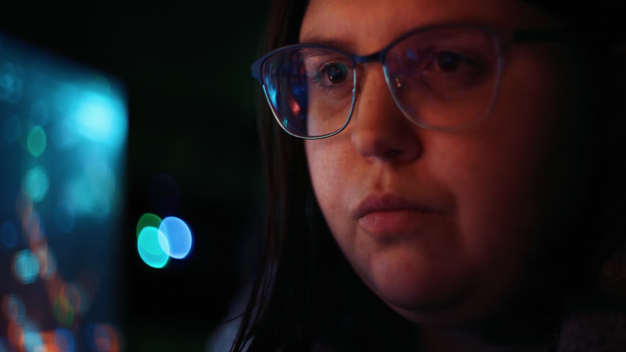 mujer adulta joven con gafas reflectantes analizando datos de código de seguridad cibernética trabajando por la noche concentrando pantallas de computadora | criptomoneda virus financiero hacker mujeres programador oscuro 4k