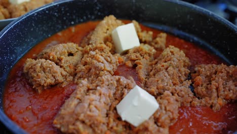 close-up of adding cubes of butter to a pan of bolognese tomato sauce while cooking