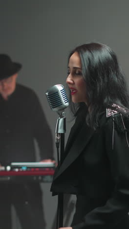 vocalista de negro canta apasionadamente en el micrófono vintage, el tecladista borroso en el fondo
