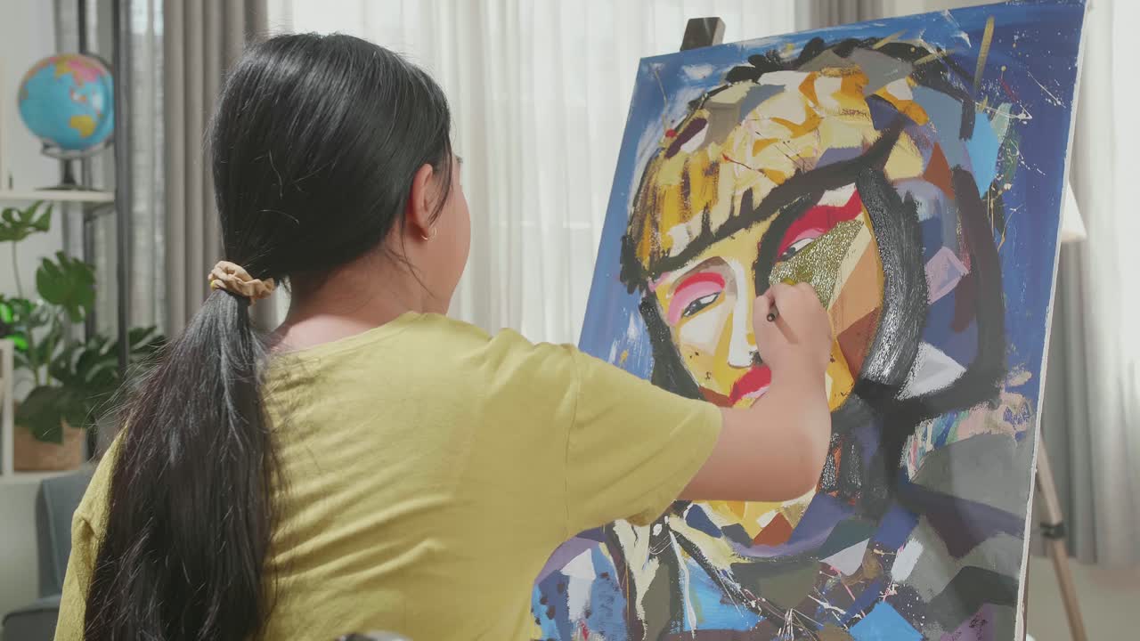 Hind View Of An Asian Artist Girl In Wheelchair Holding Paintbrush And Painting A Girl'S Face On The Canvas
