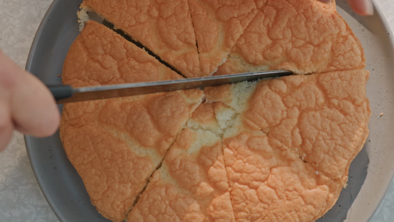 Torta soffice all'arancia affettata su piatto con coltello seghettato, vista ravvicinata dall'alto che mostra la consistenza friabile e l'interno tenero, scena di cottura casalinga con mano attenta che guida il coltello, luce naturale