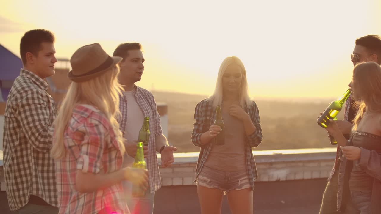 A company of young people communicates on the roof and drink beer on a summer evening