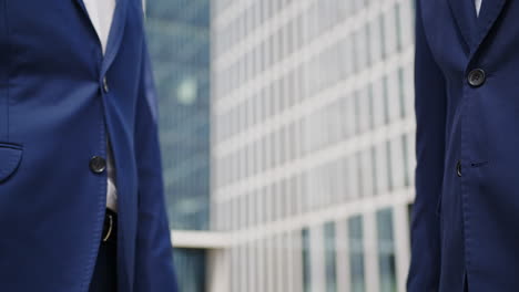 Two-business-men-with-blue-suits-shake-hands-on-successful-deal,-low-closeup