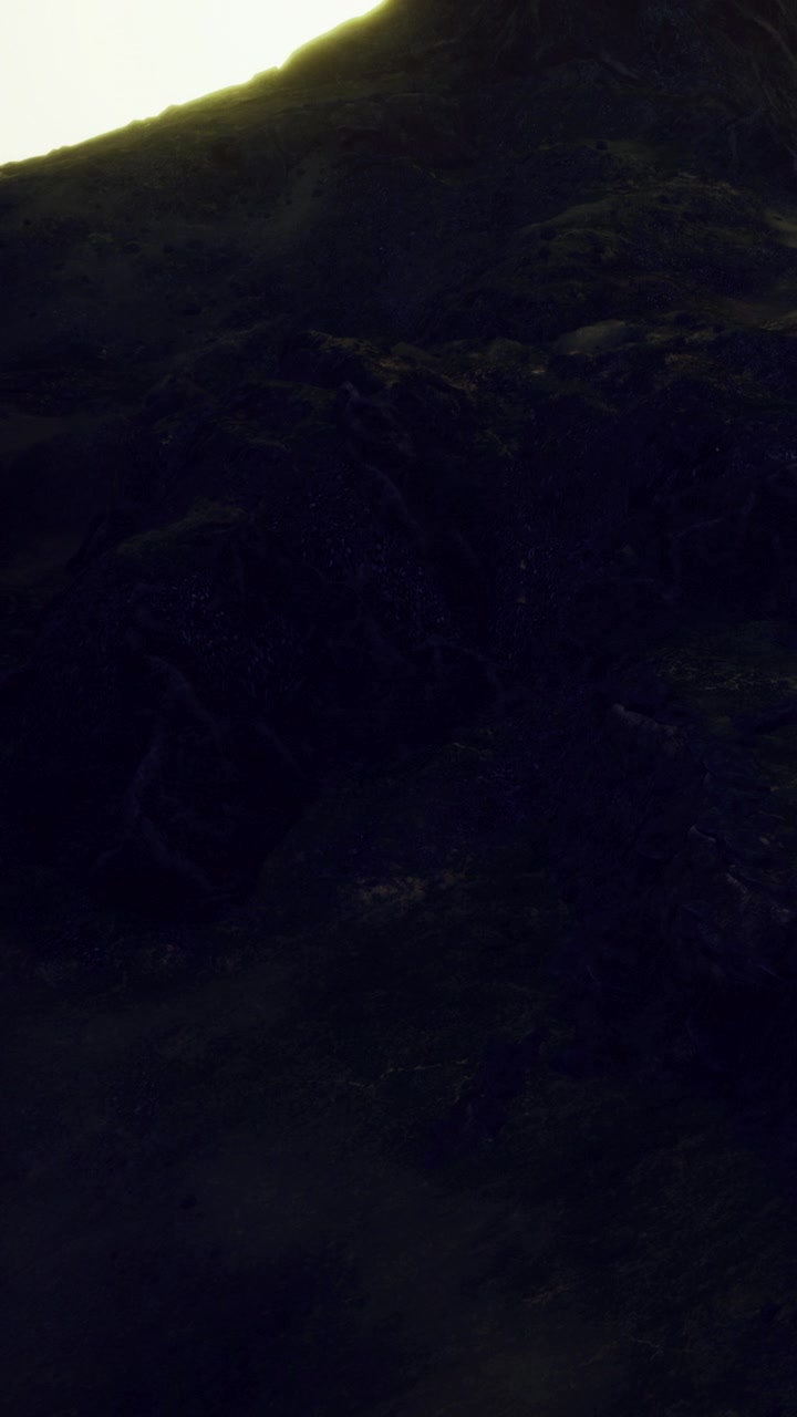 Montagne circondano un'area scura sotto il cielo notturno con poche luci visibili.