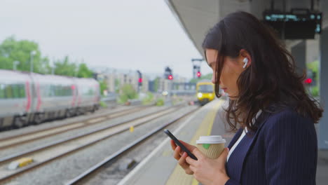 businesswoman waiting on train platform with wireless earbuds answers call on mobile phone