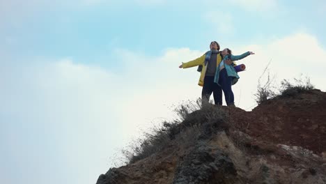 Two-hikers-standing-on-top-of-a-mountain-with-outstretched-hands-and-enjoying-the-view