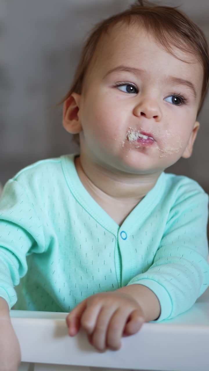 Portrait of eating small baby. Child sitting and having breakfast. Vertical video