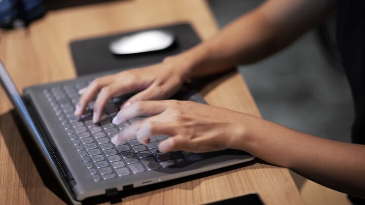 Nahaufnahme von Frauenhänden, die einen Laptop-Computer benutzen, drinnen.