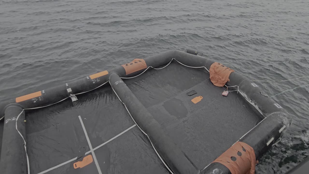 Liferaft floats on the sea near a ship hull in rainy weather. Universal emergency survival equipment