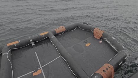 liferaft floats on the sea near a ship hull in rainy weather. universal emergency survival equipment