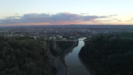 a profile aerial shot of clifton suspension bridge looking along the river avon and gorge toward the city of bristol at sunset