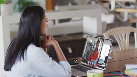 biracial businesswoman sitting at table using laptop having video call with female colleague