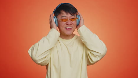 Asian-happy-man-in-headphones-listening-music-dancing-disco-having-fun-relaxing-on-christmas-party