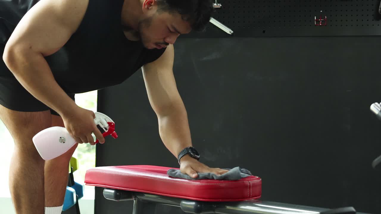 Man cleaning gym bench with spray and cloth