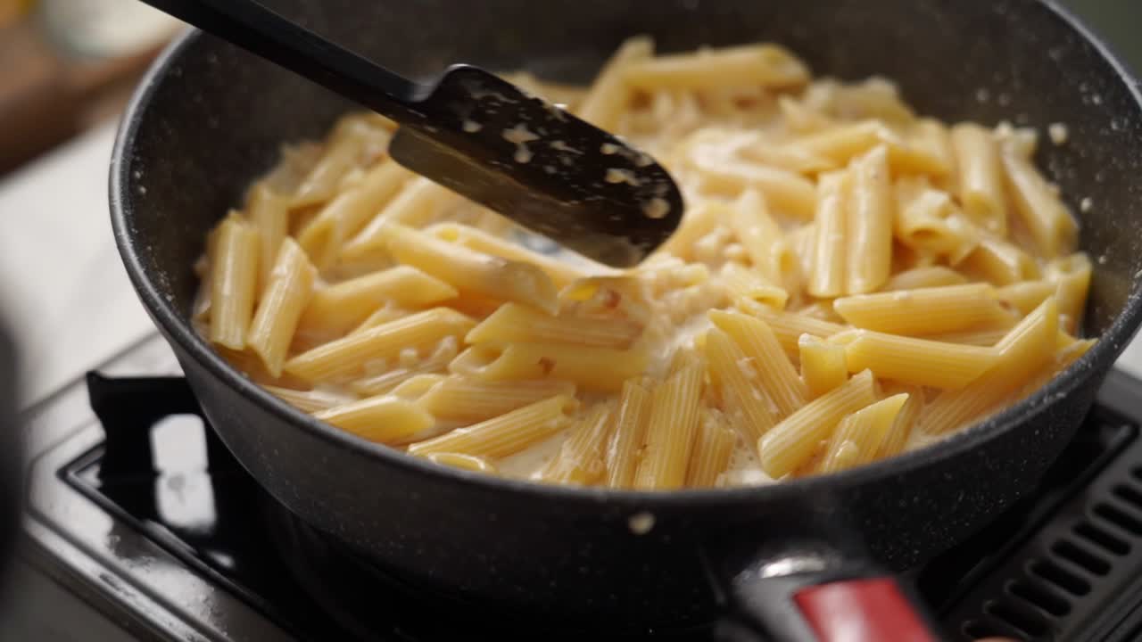 Anonymous cook stirring pasta in frying pan with spatula