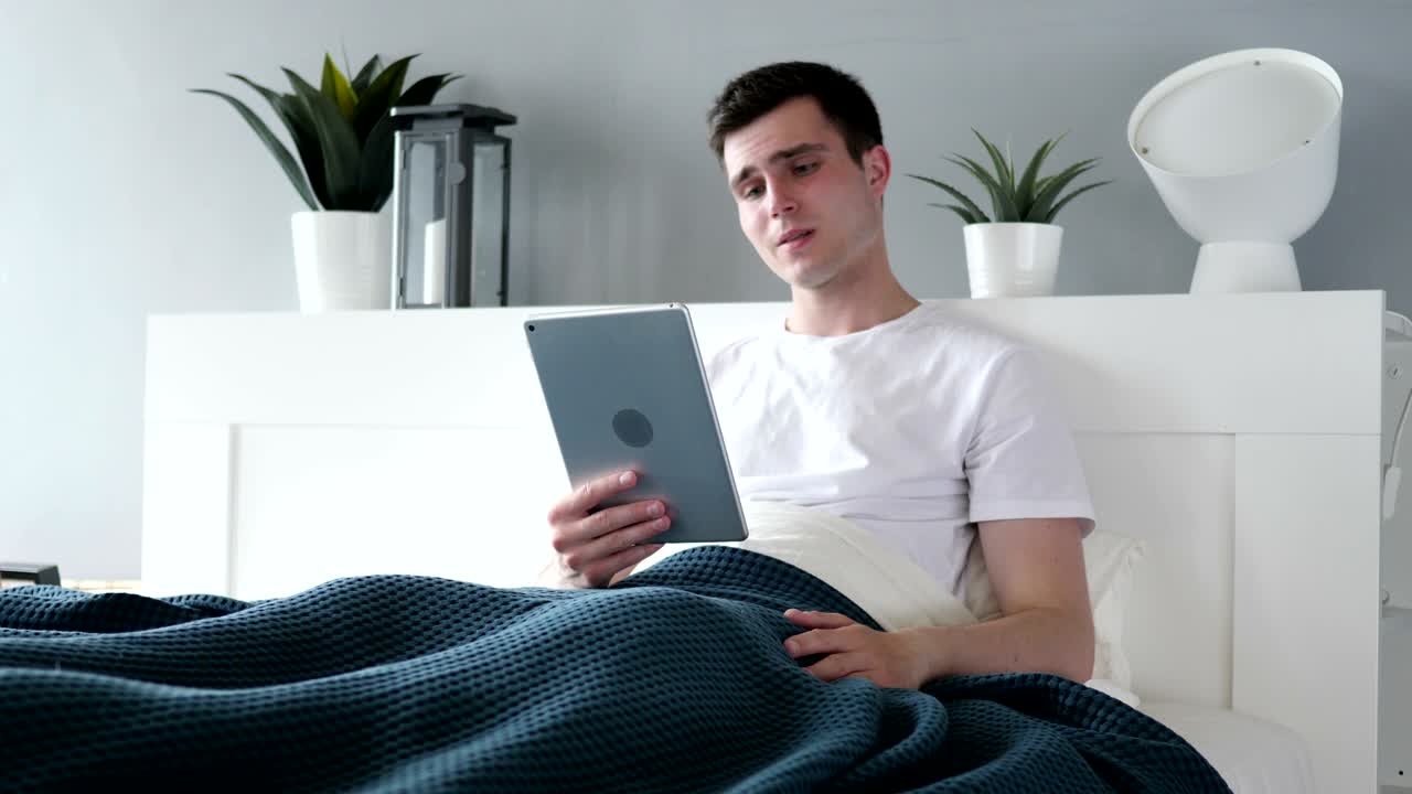 침대에서 태블릿을 사용하는 화를 내는 남자