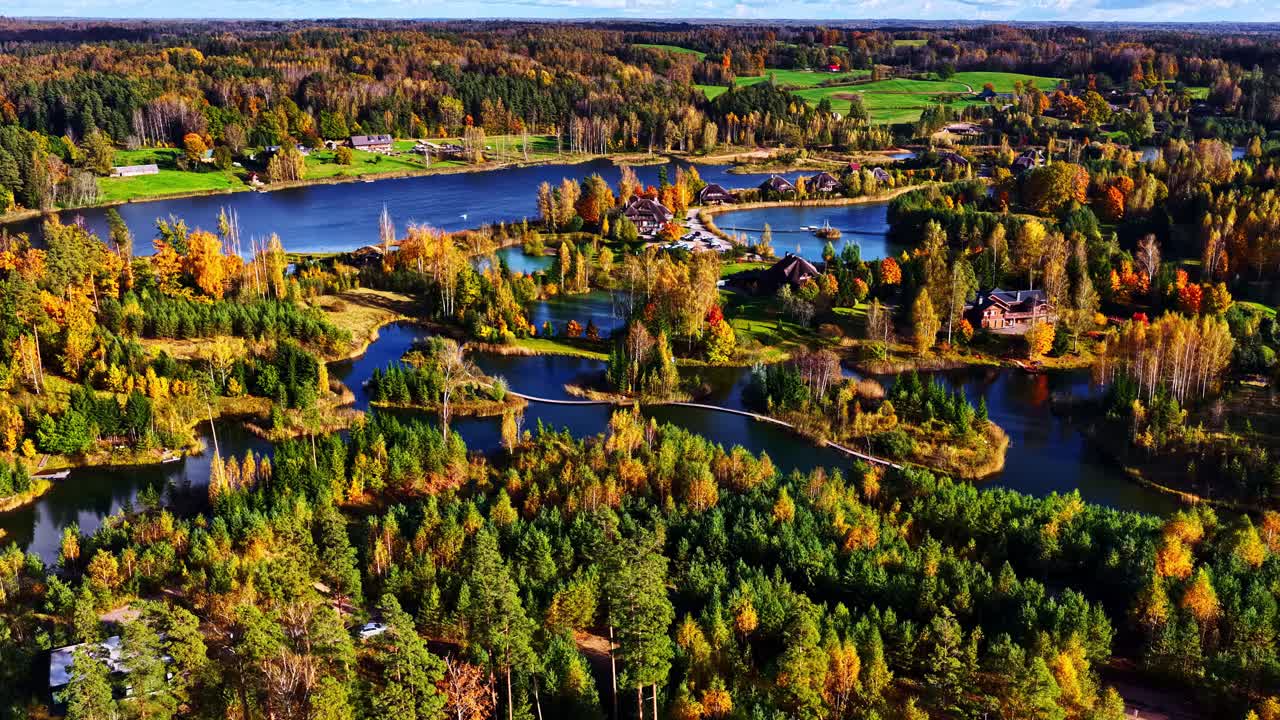 A smooth dolly shot glides forward over interconnected lakes, revealing scattered homes amid vibrant fall forests in a serene rural landscape