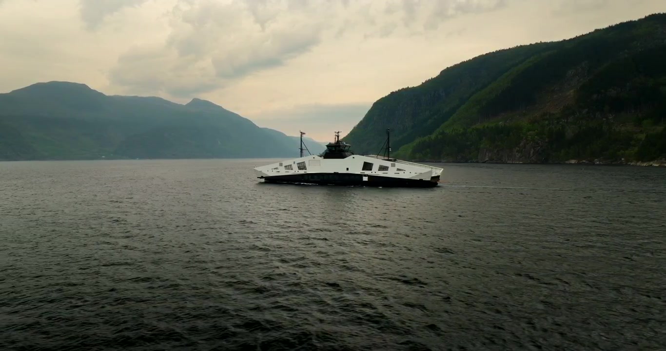 Innovativ brintbrændselscellefærge, et bæredygtigt transportfartøj, sejler på en fjord i Hjelmeland, Norge. Luftfoto fra drone med sideudsigt i lav højde, med plads til tekst