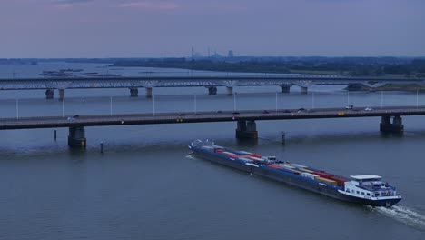 Luftaufnahme-Des-Frachtcontainerschiffs-Olesia,-Das-Sich-Der-Moerdijk-Brücke-Nähert,-Während-Abends-Der-Verkehr-Darüber-Fährt