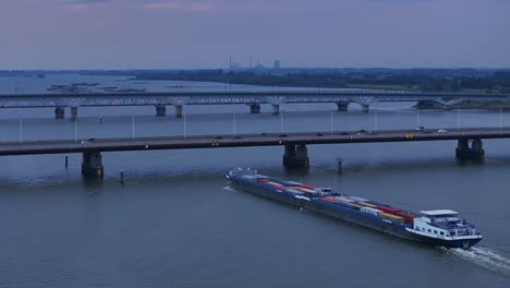 aerial view of olesia cargo container ship approaching moerdijk bridge with traffic driving across in the evening