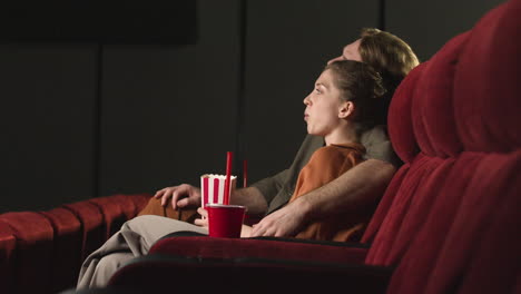 couple hugging sitting in the cinema while they watching a movie and eating popcorn