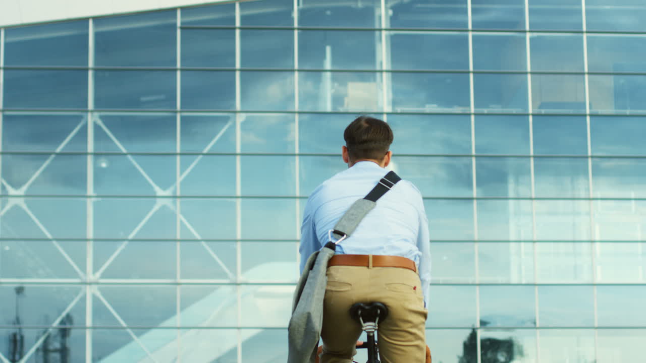 유리 건물 근처에서 자전거를 타는 캐주얼 스타일의 매력적인 남자의 뒷모습