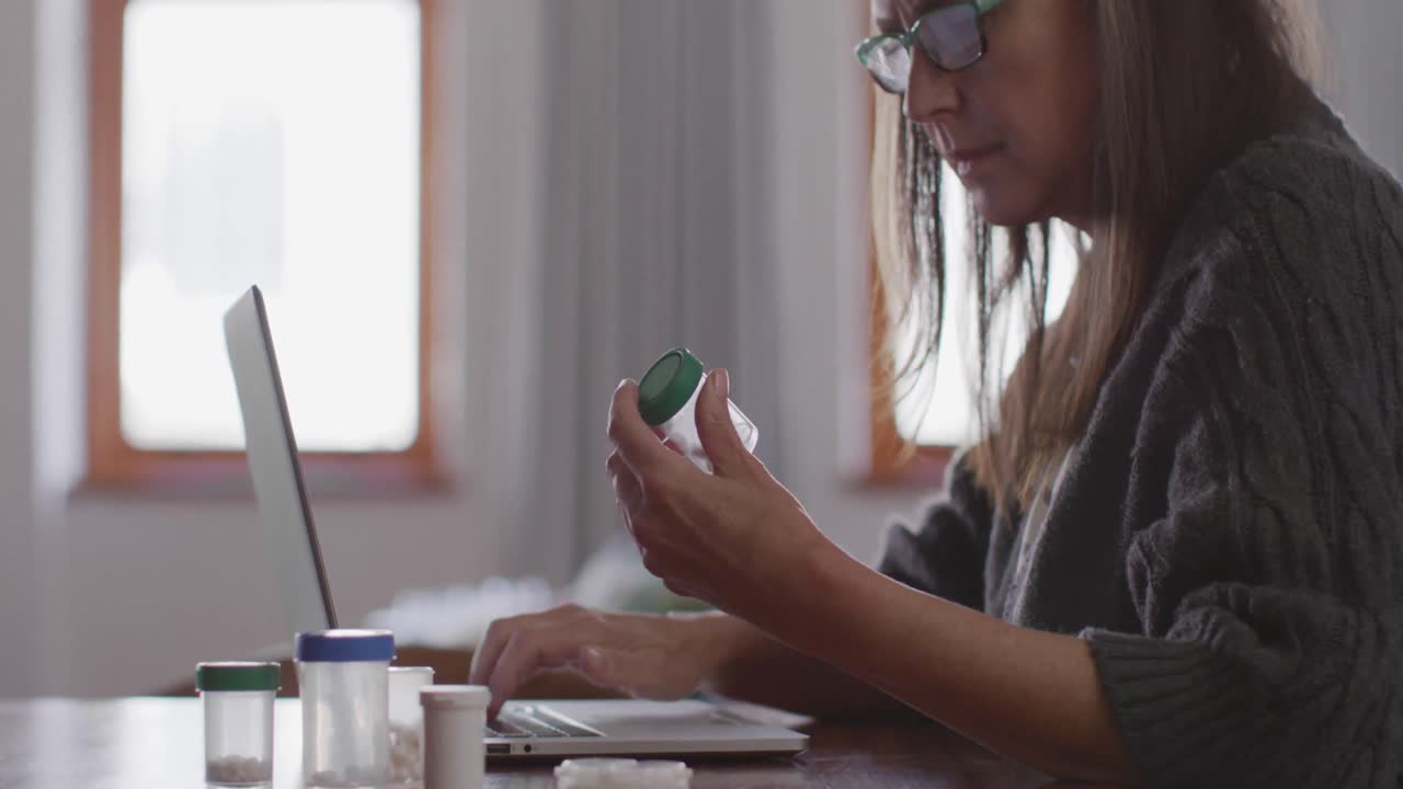 mujer con un contenedor de medicamentos y usando una computadora portátil en casa