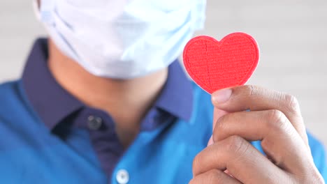 person with mask holding a red heart