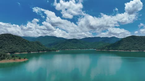 Slow-flyover-green-Feicui-Lake-with-green-mountain-range-in-background-with-clouds-at-blue-sky,-Taiwan