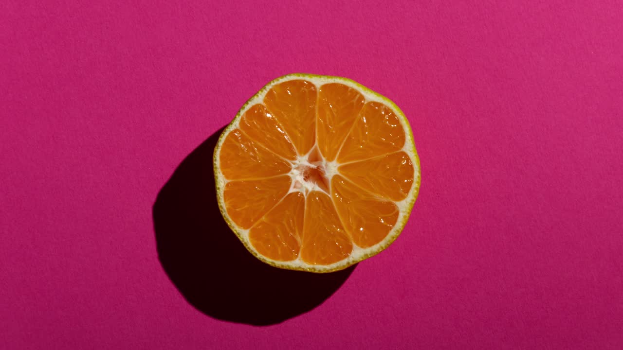 mitades de mandarina frescas con una fuerte sombra en un fondo rosado. animación de comida en stop motion
