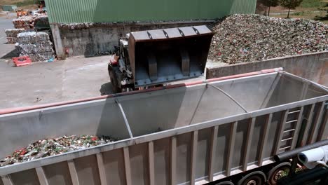 la excavadora de carretilla está bebiendo vidrio en la parte trasera de un camión transportador en el almacén, la máquina de servicio pesado tiene un brazo largo equipado con un accesorio de agarre de vidrio, vista de dron, concepto de reciclaje de vidrio