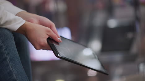 close up of hands with polished nails gently swaying tablet, showcasing subtle light reflections on screen and blurred colorful background