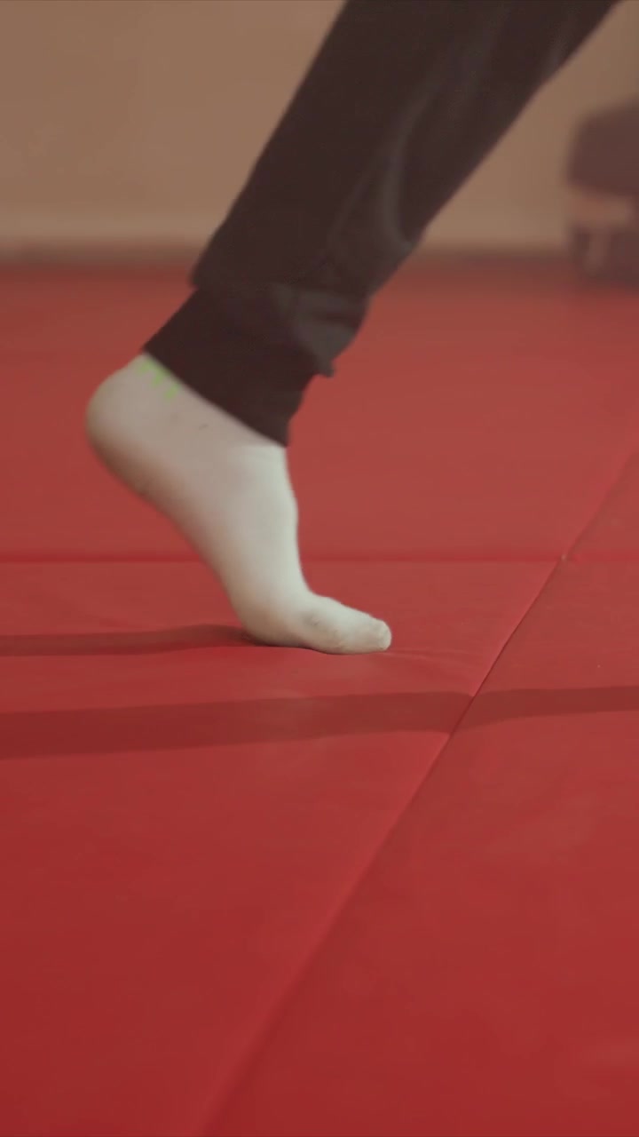 Close up of feet in socks performing various movements. Feet interact with mat showing continuous motion. Indoor setting with plain background wall visible behind subject
