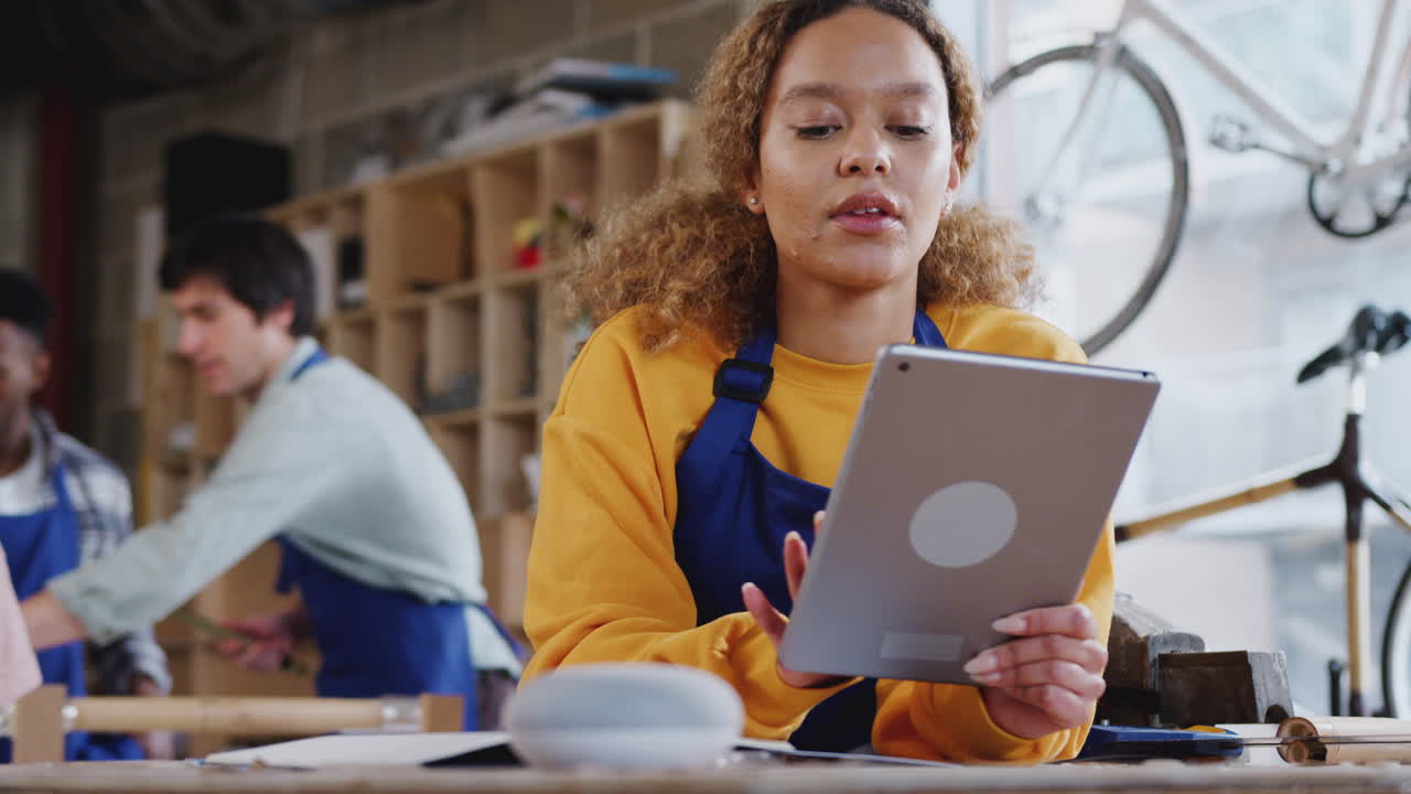 Female Worker In Carpentry Workshop Using Digital Tablet And Asking Smart Speaker Question