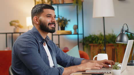 Un-Hombre-Indio-Sonriente,-Independiente,-Escribiendo-Trabajando-En-Una-Computadora-Portátil,-Escribiendo-Un-Correo-Electrónico-Importante-Desde-La-Oficina-En-Casa