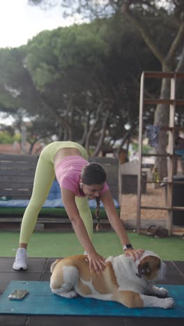 a woman stretches outdoors with her bulldog