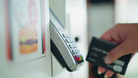 lady in pink shirt wearing a wrist chain slides a black card into a white atm machine to complete a payment transaction, with unclear items in the background, the background is blurred