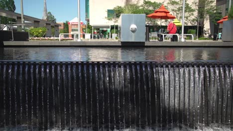 a sidetracking shot captures a waterfall cascading over a wall at whitby public library square, with contemporary architecture in the backdrop