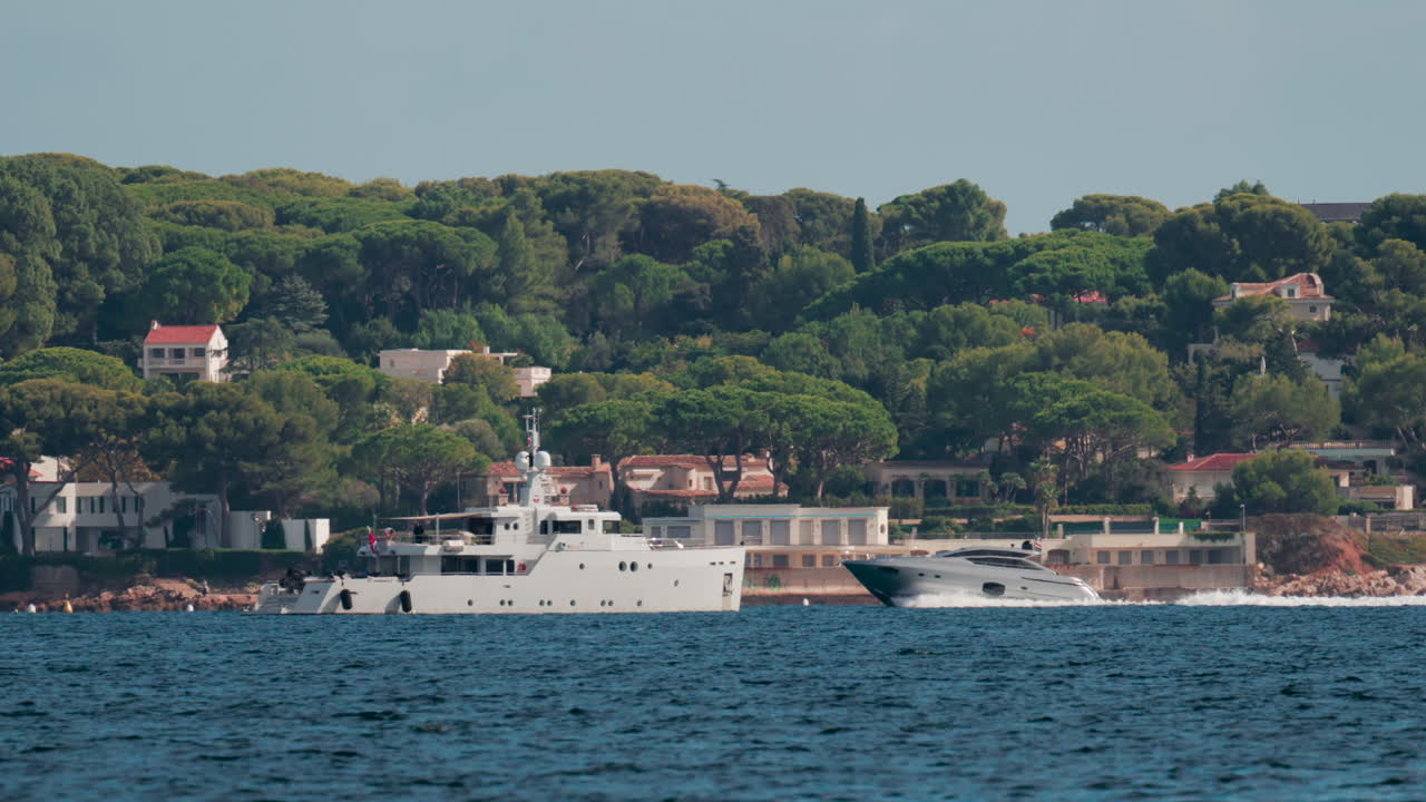 A motor yacht cruises along the coast lined with beautiful villas surrounded by green pine trees