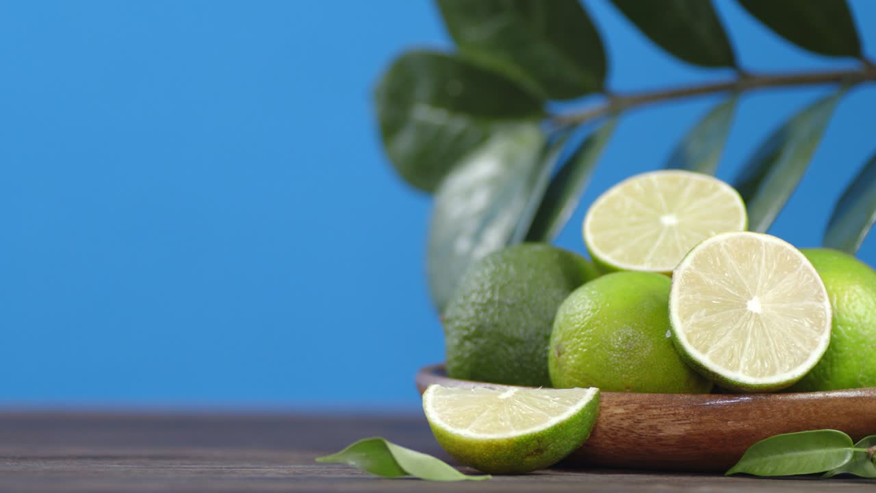 Fresh limes with leaves on wooden bowl rotate slowly.