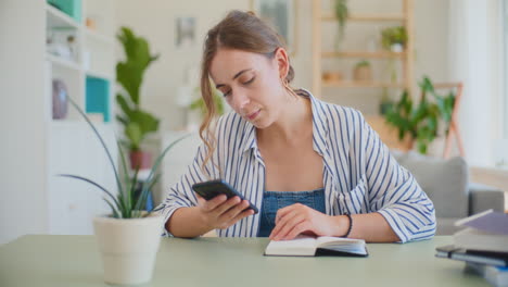 Frau-Surft-Auf-Dem-Smartphone,-Während-Sie-Am-Schreibtisch-Lernt