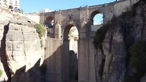 puente nuevo in ronda showing massive stone bridge over deep gorge between rocky cliffs with sunlight casting sharp shadow on canyon wall and surrounding historic architecture
