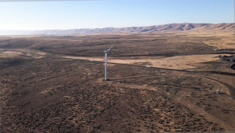 Tiro-Aéreo-Lento-De-Una-Solitaria-Turbina-Eólica-Eléctrica-Junto-A-Una-Larga-Carretera-Desértica