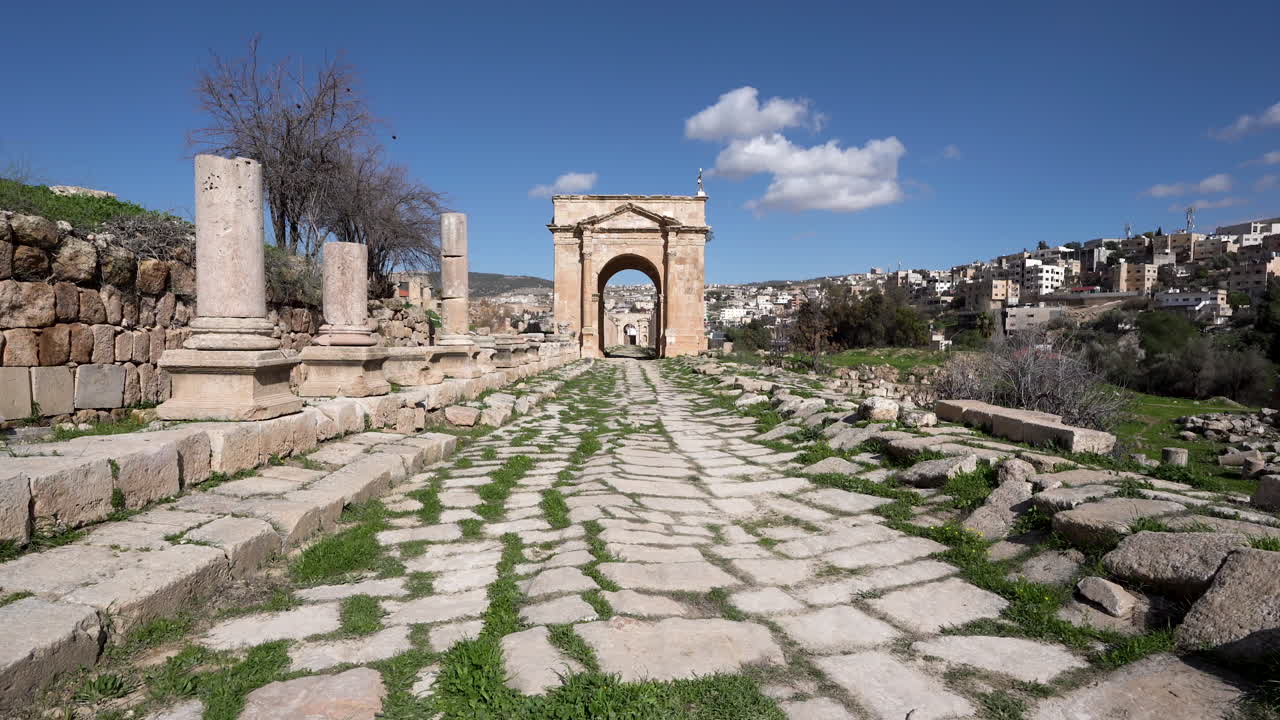 camino de piedra que conduce a una gran arquitectura con hierba que crece entre los espacios del suelo en un día soleado en ruinas romanas en jerash